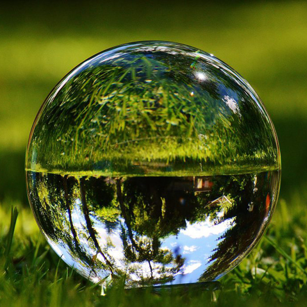 Eine auf Rasen liegende Glaskugel reflektiert Himmel, Bäume und Gräser