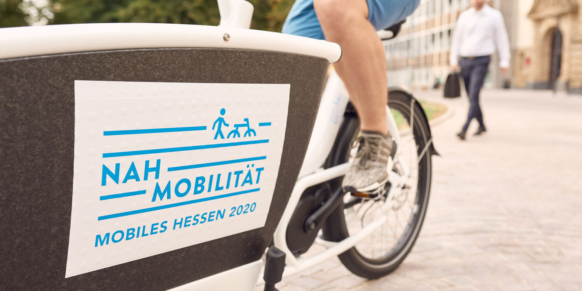 Ein Mann sitzt auf einem Fahrrad, welches die Aufschrift "Nah Mobilität Mobiles Hessen 2020" trägt.