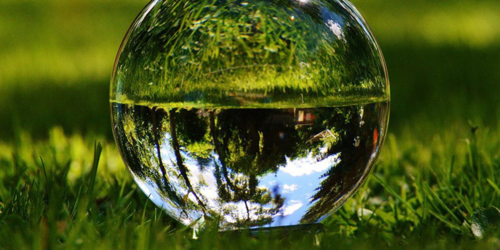 Eine auf Rasen liegende Glaskugel reflektiert Himmel, Bäume und Gräser