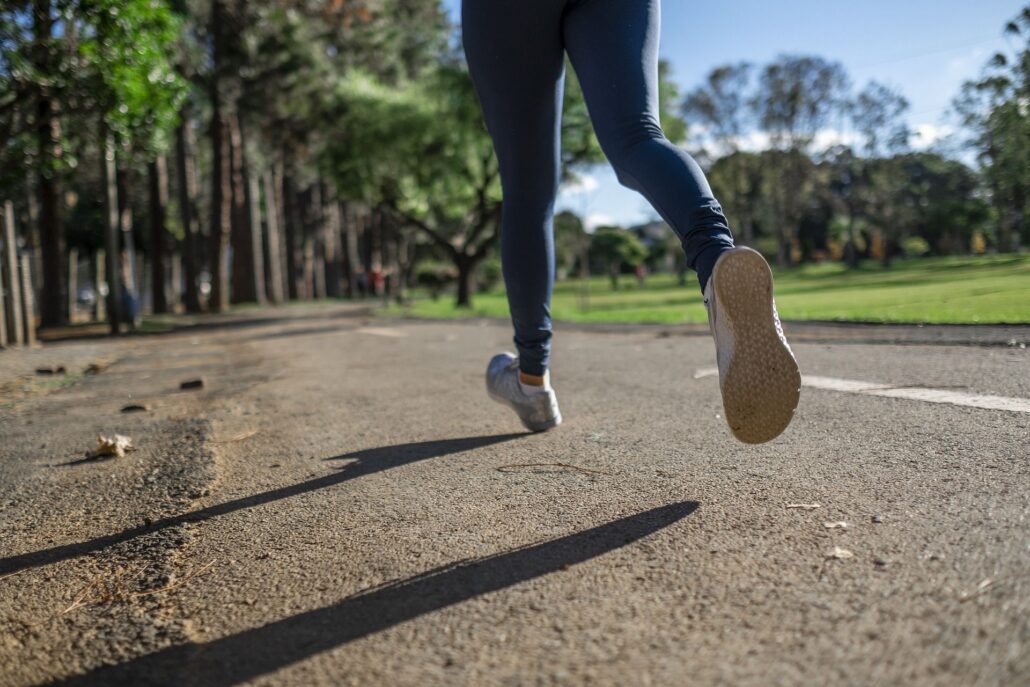 Eine Frau in Sportklamotten joggt auf einem Weg im Grünen.